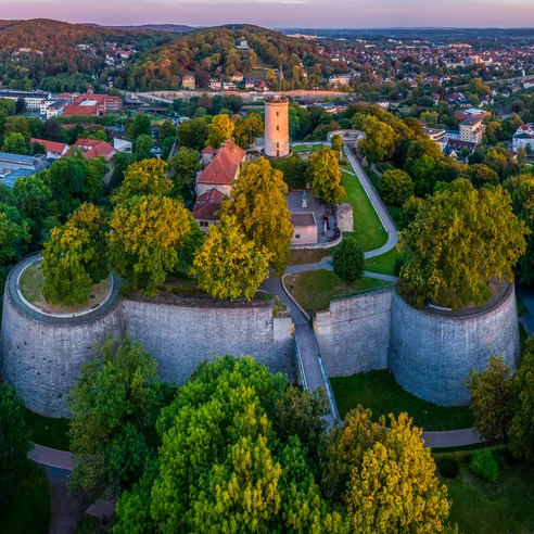 Bielefeld-Sparrenburg-Teutoburger-Wald-Tourismus-D-Ketz-009-CC-BY-SA.jpg Panoramablick auf die Sparrenburg in Bielefeld, umgeben von üppigem Grün und Stadtlandschaft.