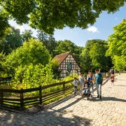 Bielefeld-Tierpark Olderdissen-Teutoburger-Wald-Tourismus-D-Ketz-024.jpg Historisches Fachwerkhaus im Grünen, umgeben von Spaziergängern auf einem sonnigen Kopfsteinpflasterweg.