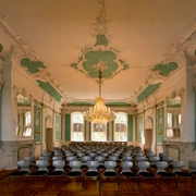 305 - Ratzeburg - Kreismuseum Rokkokosaal.jpg Im Rokokosaal des Kreismuseums stehen viele Stühle, Wände und Decke haben Stuck mit Farben, in der Mitte hängt ein Kronleuchter