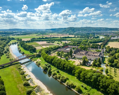 Hoexter-Corvey-Teutoburger-Wald-Tourismus-D-Ketz-061.jpg Luftaufnahme des Wesergebiets mit einem Schloss, umgeben von Wiesen, Bäumen und einem Fluss.