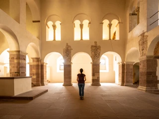 Hoexter-Corvey-Teutoburger-Wald-Tourismus-D-Ketz-054.jpg Eine Person steht in einer lichtdurchfluteten, historischen Halle mit Rundbögen und antiken Säulen.