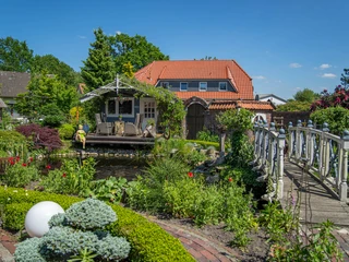 Garten_Privatgarten_Mueller Bollenhagen-17.jpg Ein liebevoll angelegter Garten mit üppigen Pflanzen, einem Teich und einer hübschen Brücke im Mittelpunkt.