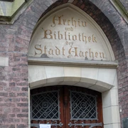 Grashaus Tür in einem steinernen Torbogen, in den in alter Schrift "Archiv und Bibliothek der Stadt Aachen" eingemeißelt ist.