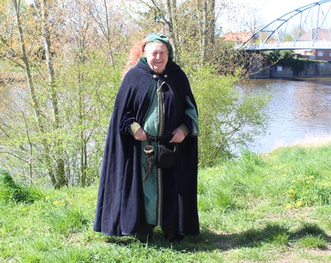 Stadtführer Nienburg  Eine mittelalterlich gekleidete Person steht vor einem Fluss, hinter einer modernen Brücke.