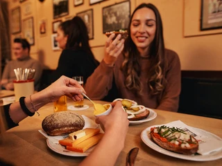 Früh im Veedel Nahaufnahme, zwei Frauen sitzen an einem Tisch gedeckt mit Mettbrötchen und Halven Hahn in einem rustikalem Brauhaus. Close-up of two women sitting at a table covered with meat rolls and “Halven Hahn” in a rustic brewery.
