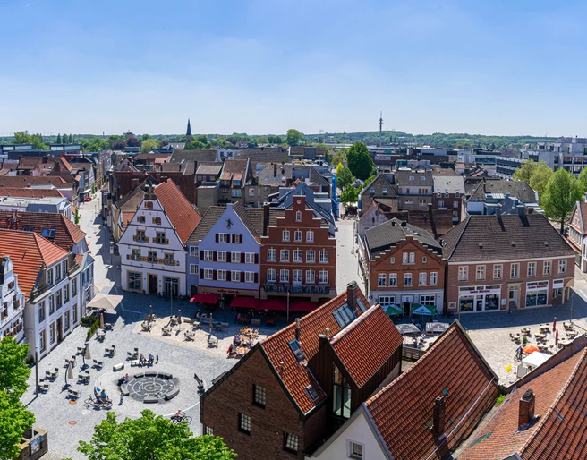 Rheine_Marktplatz03_Bildrechte EWG Rheine.jpg Panorama des belebten Marktplatzes in Rheine mit historischen Gebäuden und Menschen im Freien.