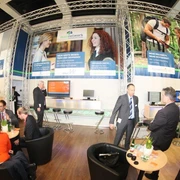 testbild Herzlich Willkommen auf einer Messe. Die Szene zeigt Menschen im Gespräch an einem Informationsstand.