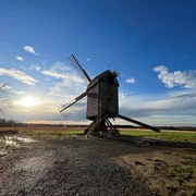 Mühle Neuenknick Historische, hölzerne Windmühle auf einem Feld bei Sonnenuntergang, umgeben von weitem Himmel und Wolken.