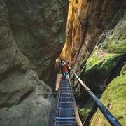 Wolfsschlucht am Hockstein  Zwei Personen steigen eine Metalltreppe in einer engen, moosbewachsenen Felsenschlucht namens Wolfsschlucht hinauf. Die Stimmung ist abenteuerlich.