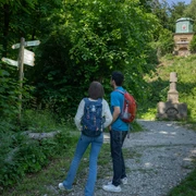 Halle-HagedornDenkmal-Teutoburger-Wald-Tourismus-Patrick-Gawandtka-088_lowres.jpg Wanderer betrachten Wegweiser vor dem Hagedorn-Denkmal im Teutoburger Wald, umgeben von üppigem Grün.