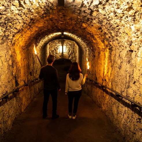 Bielefeld-Sparrenburg-Teutoburger-Wald-Tourismus-D-Ketz-024-CC-BY-SA.jpg <p>Ein Paar mit Fackeln erkundet einen historischen, beleuchteten Steintunnel. Mystische Atmosphäre.</p>