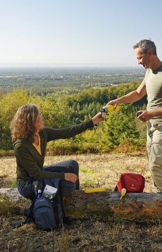 Oerlinghausen-Ausblick-ins-Lipperland-Teutoburger-Wald-Tourismus-F-Grawe (64).JPG Zwei Personen auf einer Lichtung im Teutoburger Wald, tauschen Getränke mit bewaldetem Lipperland im Hintergrund.