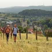 Zwei Wanderer auf einem Feldweg mit Blick auf Neuenheerse und die waldige Hügellandschaft.