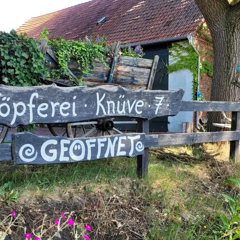 Keramikwerkstatt Sundern Töpferei im Grünen mit rustikaler Holzbeschilderung, Wagenrad und üppiger Efeubewachsung.