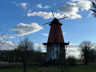 Historische Windmühle mit roter Kappe und weißen Flügeln vor blauem Himmel mit leichten Wolken.
