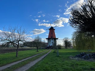 Windmühle in Diepenau-Lavelsloh mit rotem Turm und umliegendem Grün vor blauem Himmel mit Wolken.
