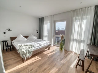 Ein helles, modernes Schlafzimmer mit einem großen Fenster, das viel Tageslicht und eine frische Atmosphäre einlässt.