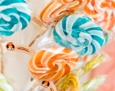 Lollis aus der Bonbonmanufaktur Bunte Lollipops in Blau-Weiß und Orange-Weiß, in Zellophan verpackt, mit Etikett "handgemachte Bonbons" auf einem Holzstiel.