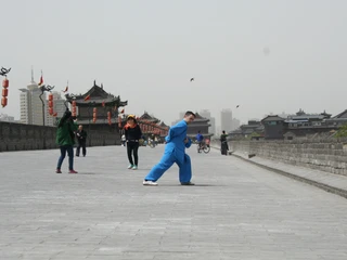 Auf der alten Stadtmauer in Xian Person in blauer Kampfkunstkleidung posiert auf einer historischen Stadtmauer; im Hintergrund sind Laternen und traditionelle Gebäude zu sehen.
