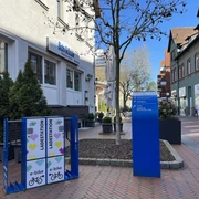 Ladestation Neustadt Ladestation für E-Bikes auf einem gepflasterten Platz vor einem Café in einer belebten Einkaufsstraße.