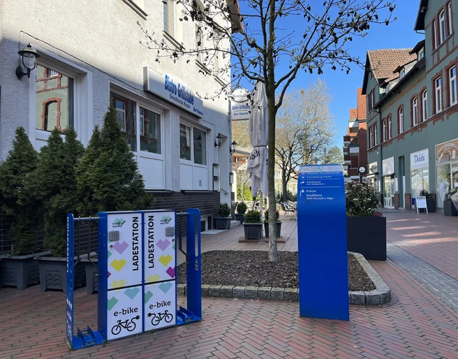 Ladestation Neustadt Ladestation für E-Bikes auf einem gepflasterten Platz vor einem Café in einer belebten Einkaufsstraße.