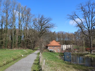 Klostermühle Heiligenberg Ein altertümliches Gebäude mit roten Ziegeln und Fachwerk, umgeben von Wiesen und einer Baumreihe.
