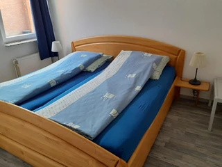 Ein Doppelbett mit blauem Bettzeug in einem hellen Zimmer, ergänzt durch zwei Nachttische mit Lampen.