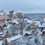 Burg Hohnstein Verschneite Burg Hohnstein thront über einem winterlichen Dorf im Elbsandsteingebirge, umgeben von Wäldern.