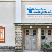 Königsteiner Lichtspiele e.V. Eingang der Königsteiner Lichtspiele e.V. mit einem Schild "Treffen, Leben, Glauben" und einem Schaukasten mit Filmankündigungen.