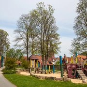 Lügde_Emmerauenpark_2416_RHa.jpg Spielplatz in einem parkähnlichen Gelände mit Piratenschiff-Klettergerüst und umstehenden Bäumen.