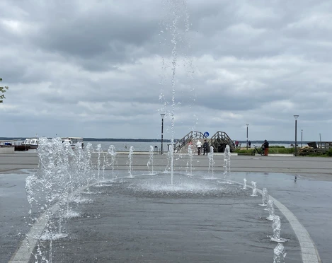 Gesamtansicht Wasserspiel_Strandterrassen Springbrunnen und Strandterrassen am Seeufer, im Hintergrund bewölkter Himmel.