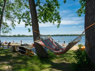 Entspannt abhängen am Kulkwitzer See Eine bunte Hängematte hängt zwischen zwei Bäumen am Ufer des Kulkwitzer Sees, während Menschen im Wasser schwimmen und am Strand entspannen.