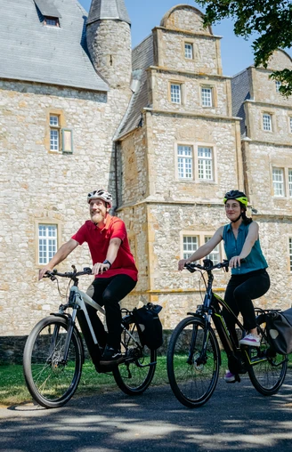 Die Schelenburg bei Bissendorf Zwei Radfahrer vor einem historischen steinernen Herrenhaus bei sonnigem Wetter.