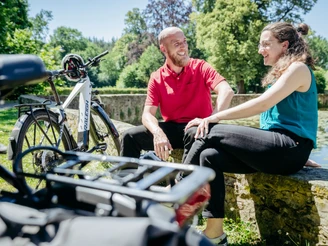 Die Schelenburg bei Bissendorf Lächelndes Paar sitzt auf einer Steinmauer, neben einem E-Bike im grünen Park.