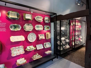Spargelmuseum Vitrinen mit historischen Spargeltellern und Besteck setzen farbliche Akzente auf magentafarbenem Hintergrund.