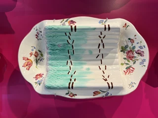 Spargelmuseum Ein kunstvoll bemalter Porzellanteller ausgestellt auf einem kräftig pinkfarbenen Hintergrund.