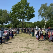troedelmarkt-mardorf-staende.jpg Trödelmarkt in Mardorf, Besucher stöbern zwischen Verkaufsständen im Freien, umgeben von Bäumen.