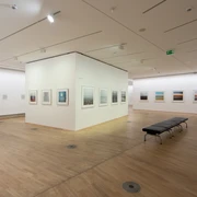 The Photographic Collection/SK Stiftung Kultur Ein lichtdurchfluteter Ausstellungsraum in einer Galerie mit Holzfußboden, an dessen Wänden gerahmte Fotografien hängen.A light-flooded exhibition space in a gallery with a wooden floor and framed photographs hanging on the walls.