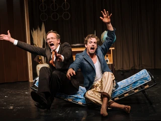 Theater im Bauturm Zwei Schauspieler in dramatischer Pose auf Bettenrahmen. Einer im Anzug, der andere leger. Two actors in dramatic poses on bed frames. One in a suit, the other casual.