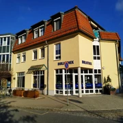 Stadtbibliothek Neustadt in Sachsen  Gelbes Gebäude mit rotem Dach, beschriftet mit "Bibliothek", bei sonnigem Wetter; Fahrradständer und Verkehrsschilder im Vordergrund.