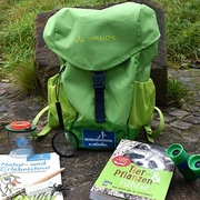 Entdeckerrucksack am Naturerlebnispfad in Monheim am Rhein Ein grüner Rucksack mit Büchern, einer Lupe und einem Fernglas liegt auf einem Naturpfad.