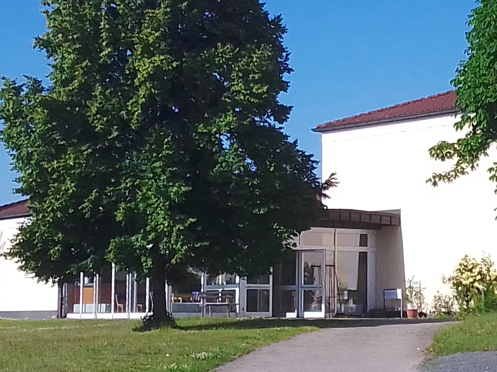 Sport-und Freizeittreff Reinhardtsdorf-Schöna Ein modernes Gebäude mit großen Fenstern, umgeben von grünen Bäumen und Rasen, unter einem klaren blauen Himmel.
