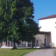 Sport-und Freizeittreff Reinhardtsdorf-Schöna Ein modernes Gebäude mit großen Fenstern, umgeben von grünen Bäumen und Rasen, unter einem klaren blauen Himmel.