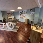 Ausstellungsraum mit historischen Werkzeugen und Infotafeln auf Holzboden, Fokus auf großen Holzwagen.