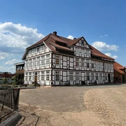 Rittergut von Behr Hoya Fachwerkhaus mit rotem Dach, umgeben von gepflastertem Hof unter blauem Himmel mit Wolken.
