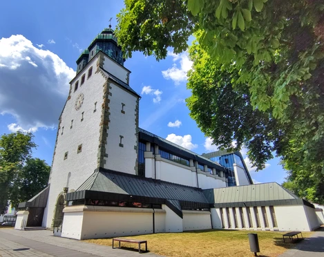 Weiße Kirche mit grünem Turm, flankiert von Bäumen, unter wolkenlosem, blauem Himmel in Hövelhof.