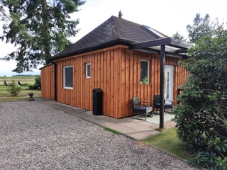 Ferienhaus Max Holzverkleidetes Ferienhaus mit steilem Dach, umgeben von Bäumen und Kiesweg, lädt zur Erholung ein.