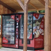 Proviantomat in Pfaffendorf Roter Verkaufsautomat mit Snacks und Getränken unter einem hölzernen Unterstand, umgeben von ländlicher Umgebung.