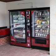Proviantomat in Gohrisch Zwei rote Verkaufsautomaten stehen nebeneinander; der linke bietet Getränke, der rechte Snacks und Lebensmittel an. Daneben eine rote Kühlbox.