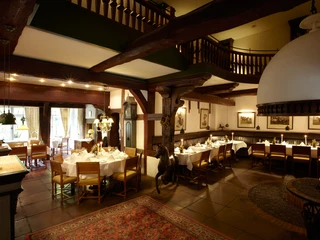 Rustikales Restaurant mit Holzbalkon, gedeckten Tafeln und einem Kamin im gemütlichen Innenraum.